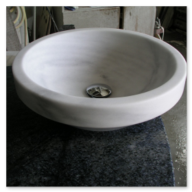 Detailansicht eines runden, aus einem Block gefrästen Waschbeckens aus weißem Marmor.