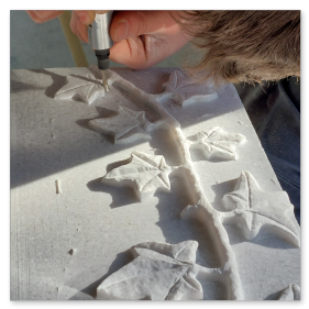 Steinmetzmeister bei der feinen Ausarbeitung eines floralen Ornaments mit Meißel und Knüpfel.