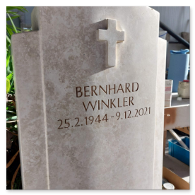 Nahaufnahme eines kleinen Kreuz-Reliefs auf fein geschliffenem Naturstein.