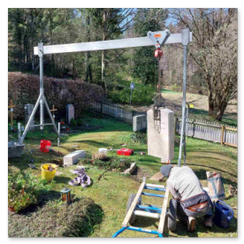 Ein Grabstein schwebt am Portalkran sicher über einen schmalen Friedhofsweg.