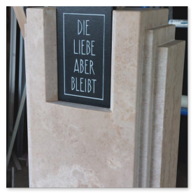Moderne Natursteinstele mit der eingehauenen Inschrift „Die Liebe aber bleibt“.